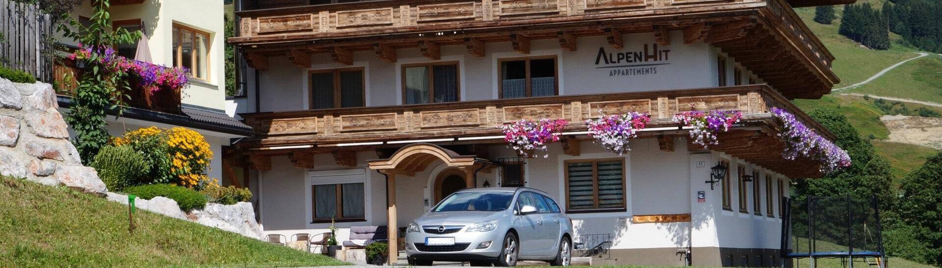 Appartementhaus AlpenHit Saalbach mit Blumenbalkonen und Bergpanorama im Sommer