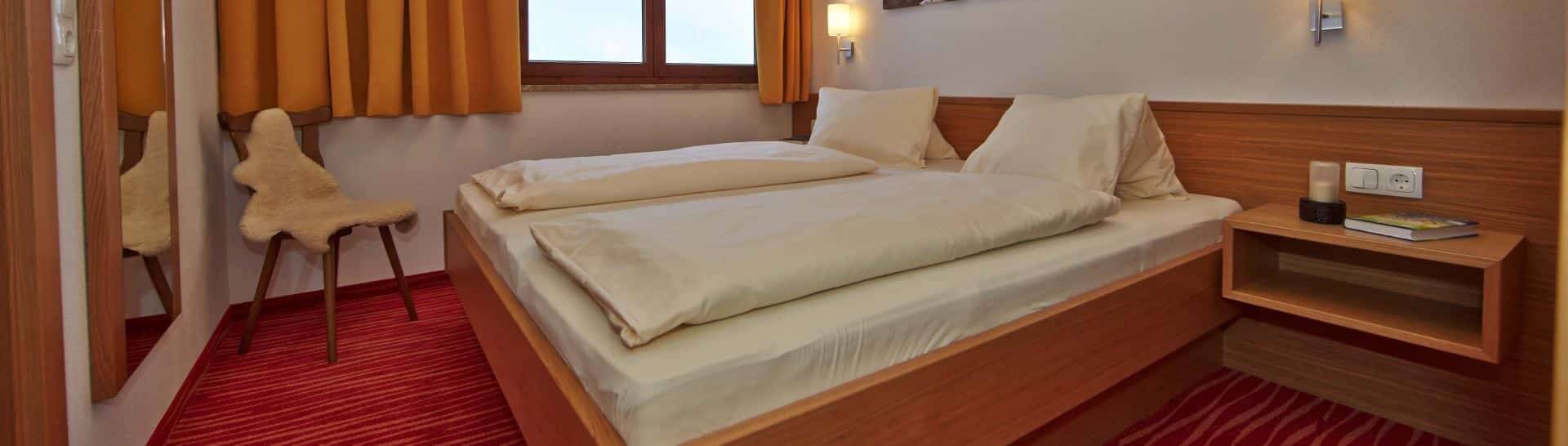 Doppelbett im Appartement Saalbach mit Holzoptik, roter Teppich, Fenster, Nachttisch