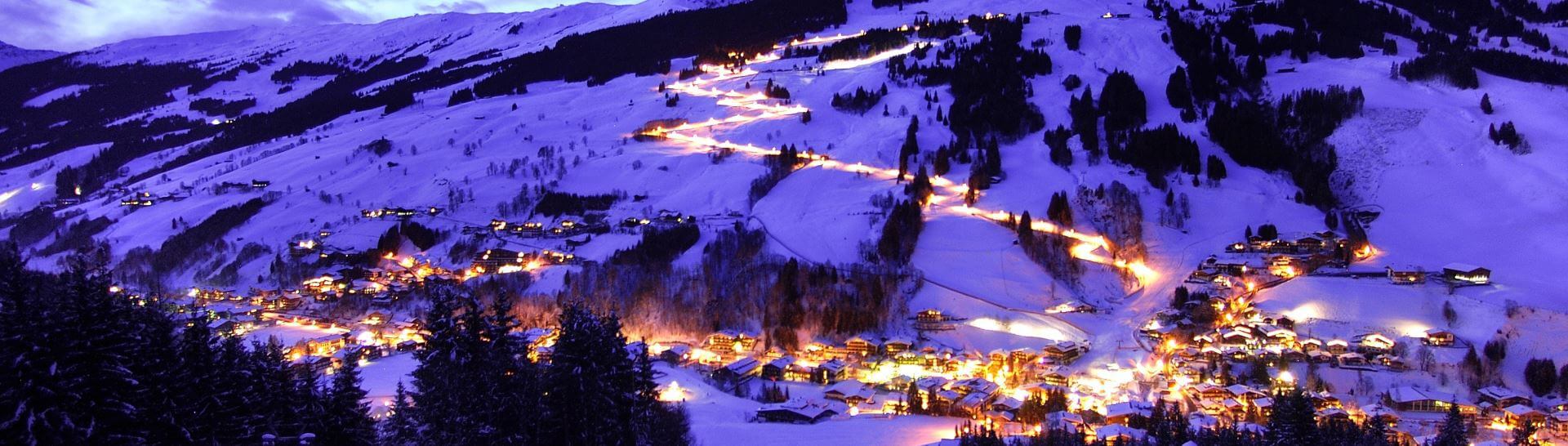 Winterliches Alpenpanorama mit beleuchtetem Dorf und Skipiste in Saalbach bei Nacht