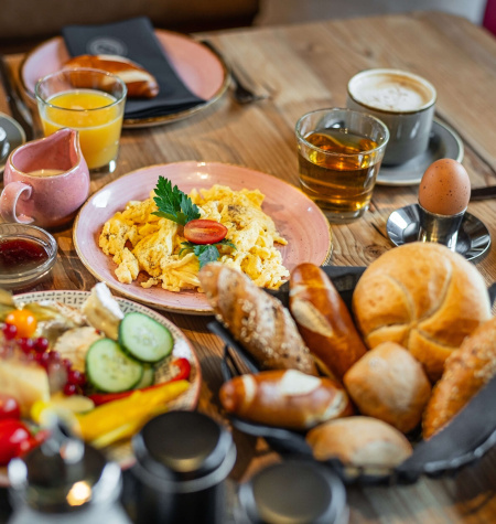 Vielfältiges Frühstück mit Eierspeise, Obst, Brot und Getränken in gemütlicher Atmosphäre.