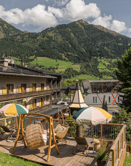 Holzterrasse mit Hängesesseln und Sonnenschirmen vor grünen Berghängen