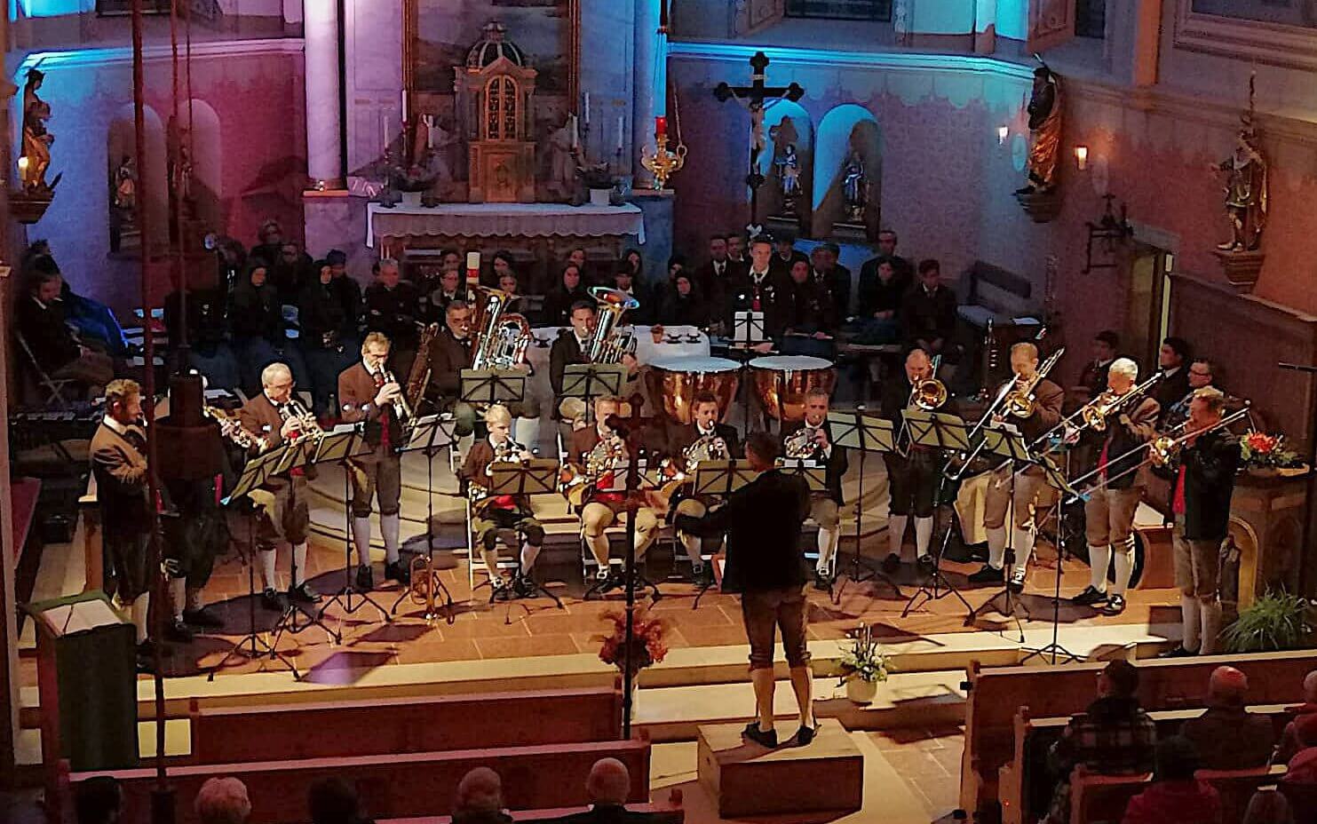 Blasmusikaufführung in einem festlichen Raum mit Musizierenden und Publikum.