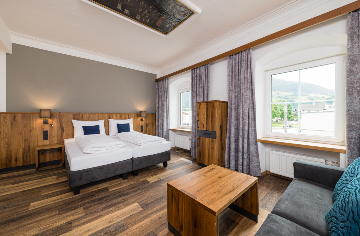 Modernes Hotelzimmer mit Doppelbett, Holzmöbeln, Sofa und Blick auf grüne Berge