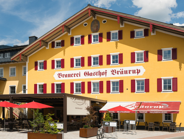 Gelbes traditionelles Hotel mit rotem Schriftzug und Terrasse im Salzburger Land