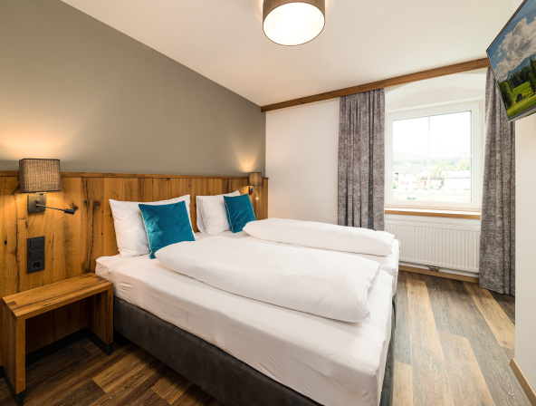 Modernes Doppelzimmer mit Holzmöbeln, Parkettboden, großem Fenster und TV
