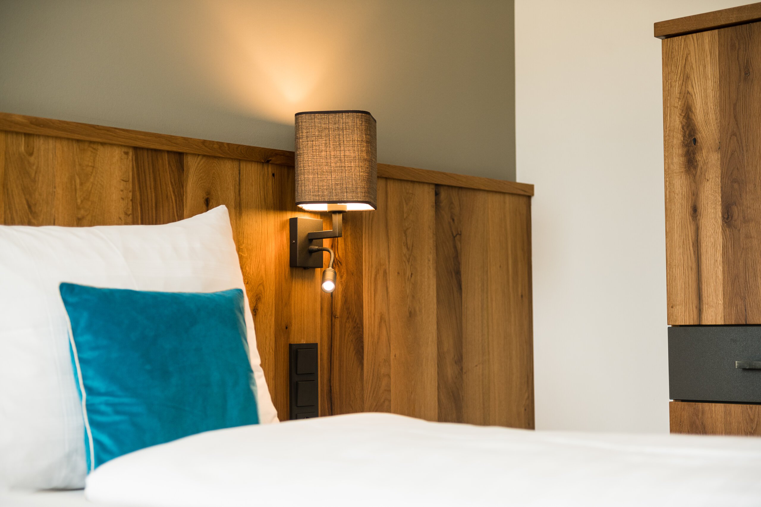 Modernes Hotelzimmer mit Holzmöbeln, weißer Bettwäsche und türkisfarbenem Kissen