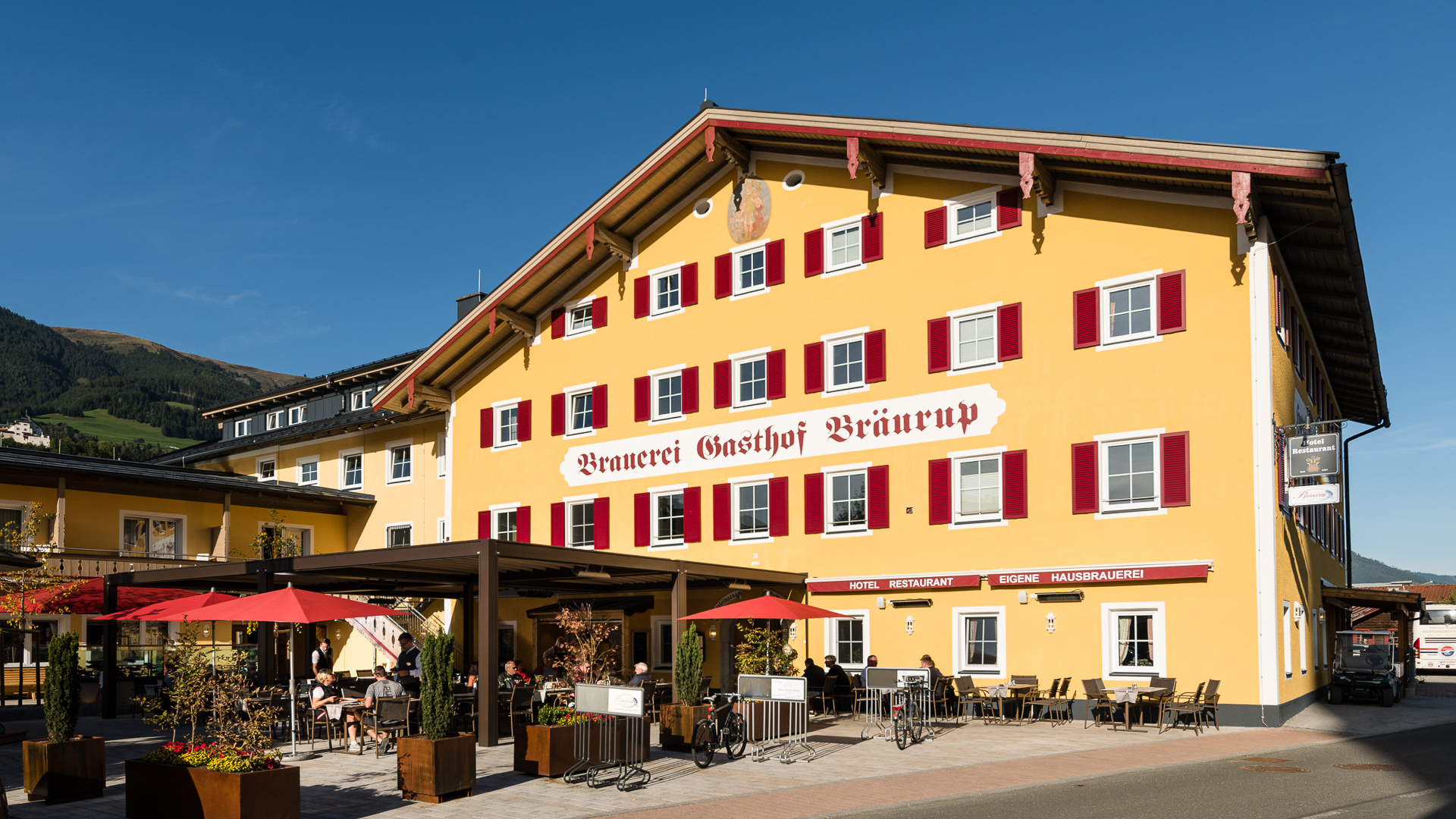 Gelbes Traditionshotel mit rotem Schriftzug und Sonnenterrasse im Salzburger Land