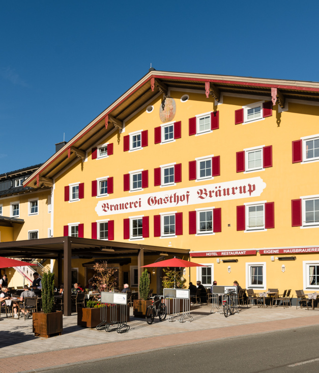 Gelbes Traditionshotel mit rotem Schriftzug und Sonnenterrasse im Salzburger Land
