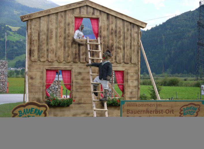 Holzhaus mit Strohpuppe und Bauernherbst-Schild in Mittersill