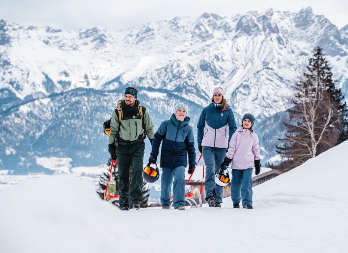 Familie wandert mit Schlitten im verschneiten Gebirge