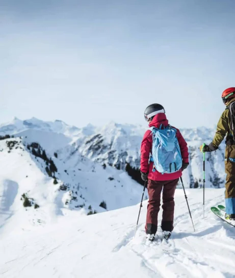 Zwei Skifahrer auf verschneitem Berggipfel mit Alpenpanorama