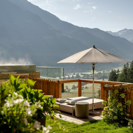 Sonnige Spa-Terrasse mit Liegen und Sonnenschirm vor weitem Blick auf Tal und Berge