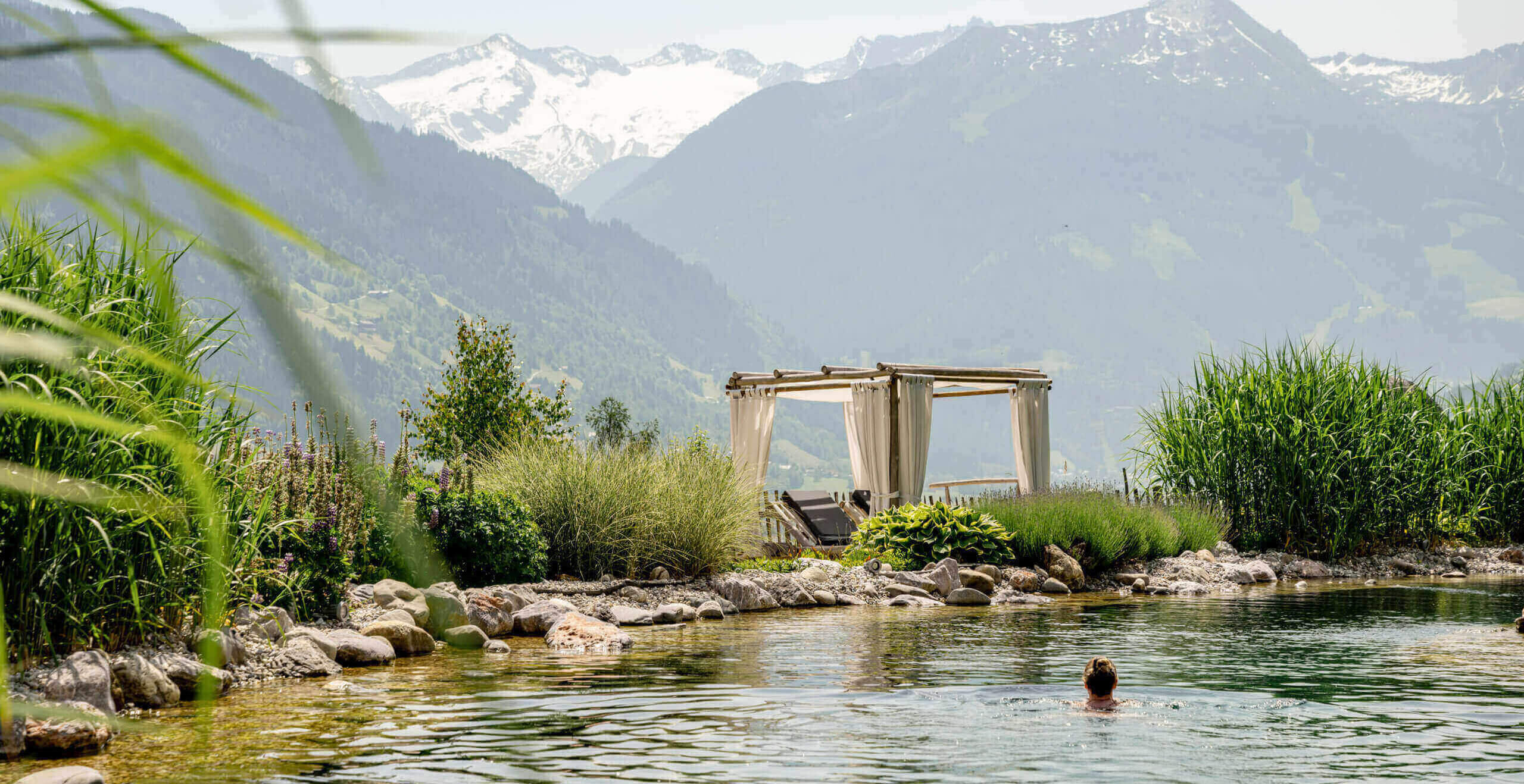 Naturbadesee mit Liegefläche vor Bergpanorama im Wellnesshotel DAS.GOLDBERG Salzburg