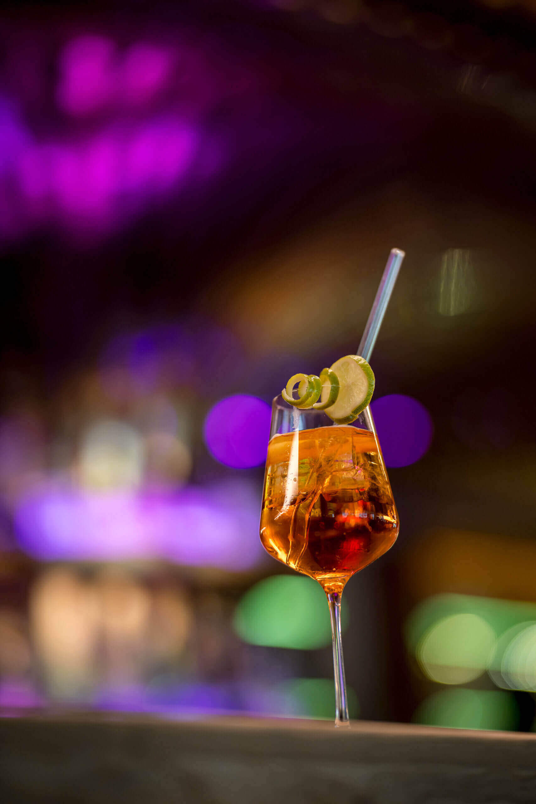 Cocktail mit Limettenscheibe vor stimmungsvoller Bar im Designhotel Bad Hofgastein