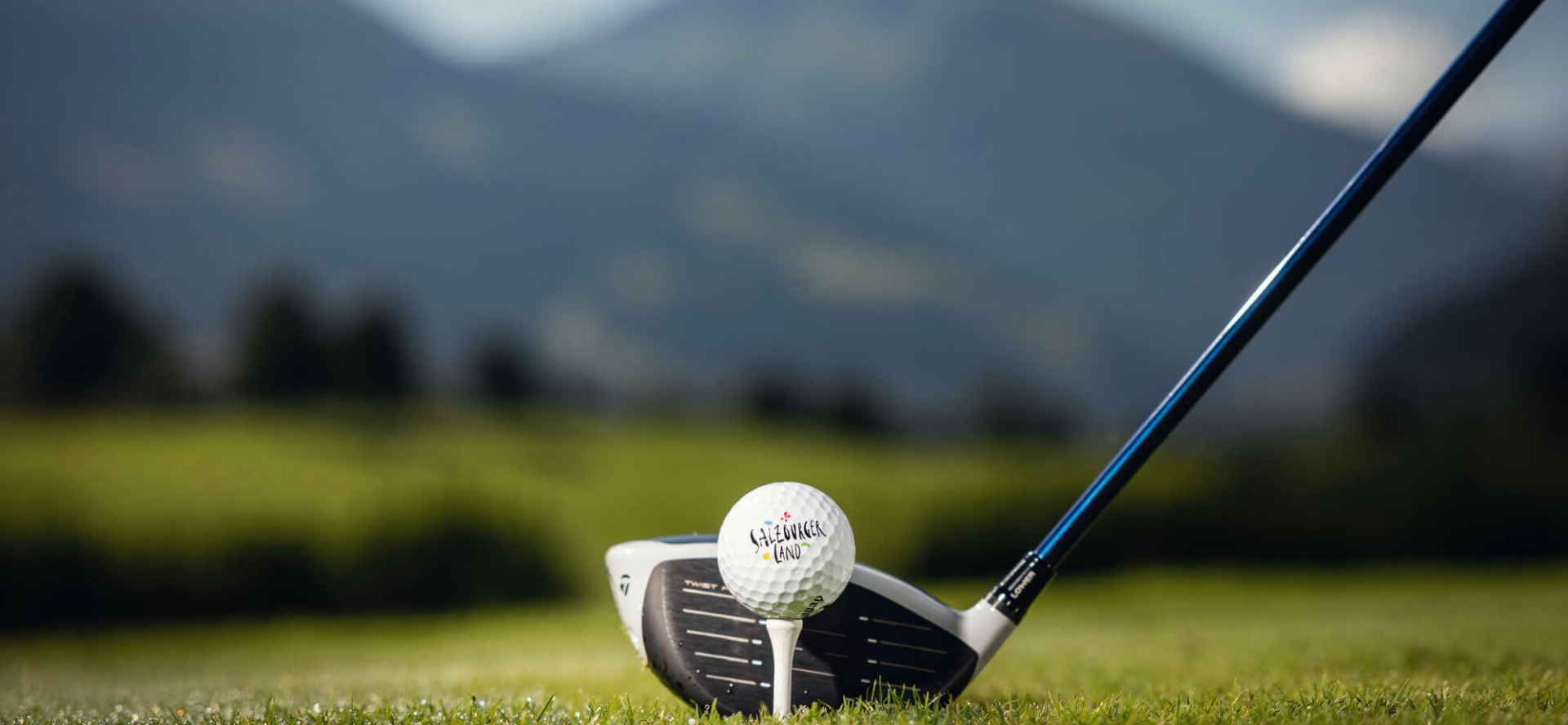 Golfball auf Abschlag mit Golfclub vor Bergpanorama im Salzburger Land Wellnesshotel