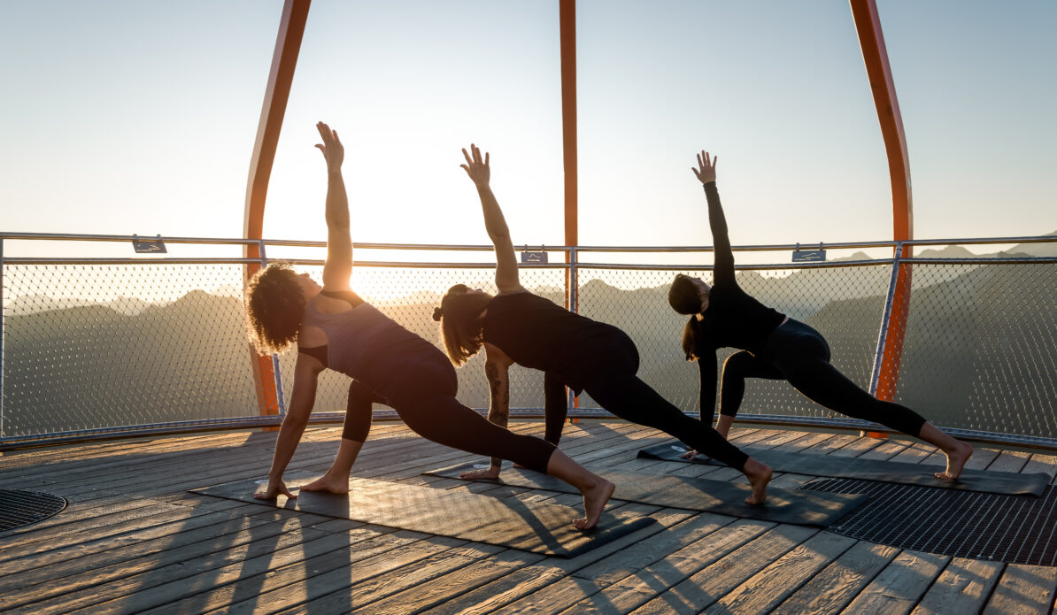 Drei Personen machen Yoga bei Sonnenaufgang in den Bergen