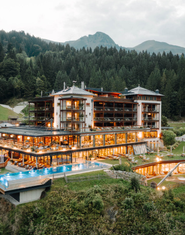 Beleuchteter Hotelkomplex auf einem Hang vor bewaldeten Bergkuppen