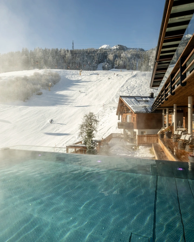 Beheizter Infinity Pool mit Blick auf verschneite Skipisten und Berge