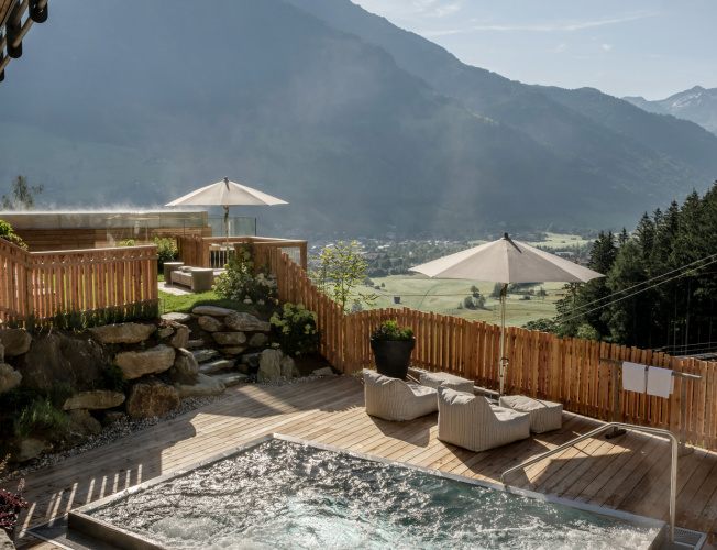 Beheizter Outdoor-Whirlpool auf Holzterrasse mit Liegen, Sonnenschirmen und Bergblick