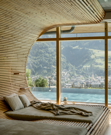 Ruheliegen aus Holz im Spa vor Panoramafenstern mit Blick auf einen Außenpool und das Tal