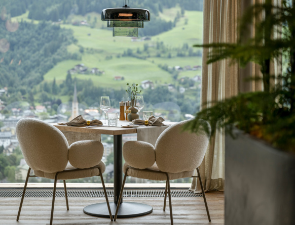 Gedeckter Tisch für zwei vor großem Fenster mit Blick auf grünes Bergtal