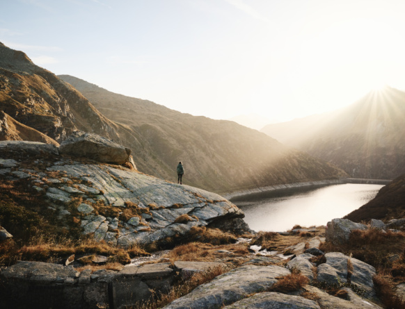 Wanderer auf felsigem Bergplateau über einem See im Sonnenlicht