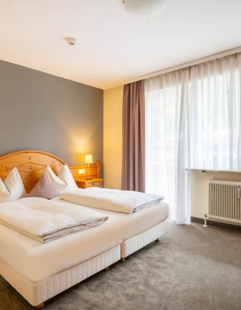 Helles Schlafzimmer mit Doppelbett, Nachttischen, Vorhängen und großem Fenster in Bad Hofgastein