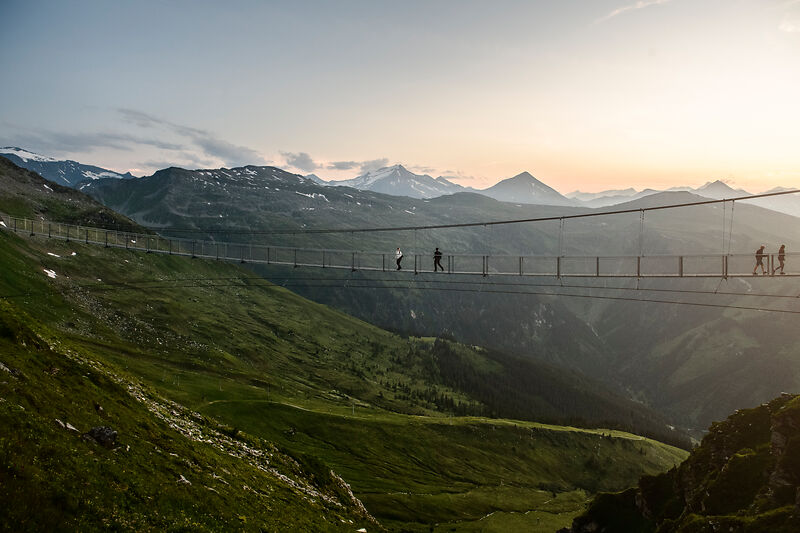 Hängebrücke mit Wanderern vor Alpenpanorama im Gasteinertal bei Sonnenuntergang