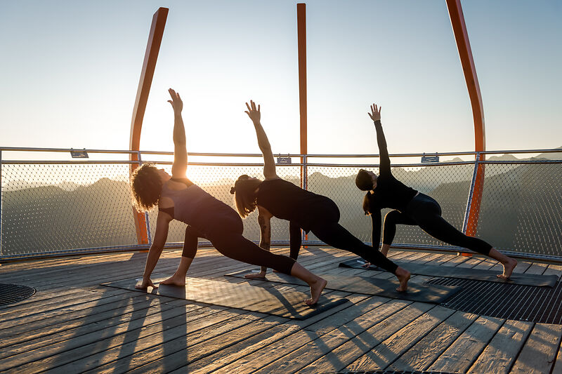 Drei Personen machen Yoga bei Sonnenaufgang mit Alpenpanorama im Gasteinertal