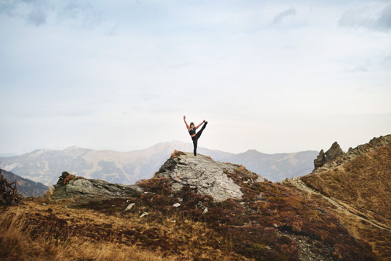 Frau macht Yoga auf Felsen in den Alpen mit Bergpanorama im Gasteinertal