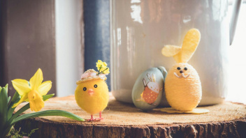 Osterdeko mit gelbem Küken, Hase und Narzisse auf einer Holzscheibe