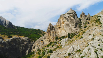 Helle Felsformationen mit grünen Sträuchern in einer bergigen Landschaft unter bewölktem Himmel