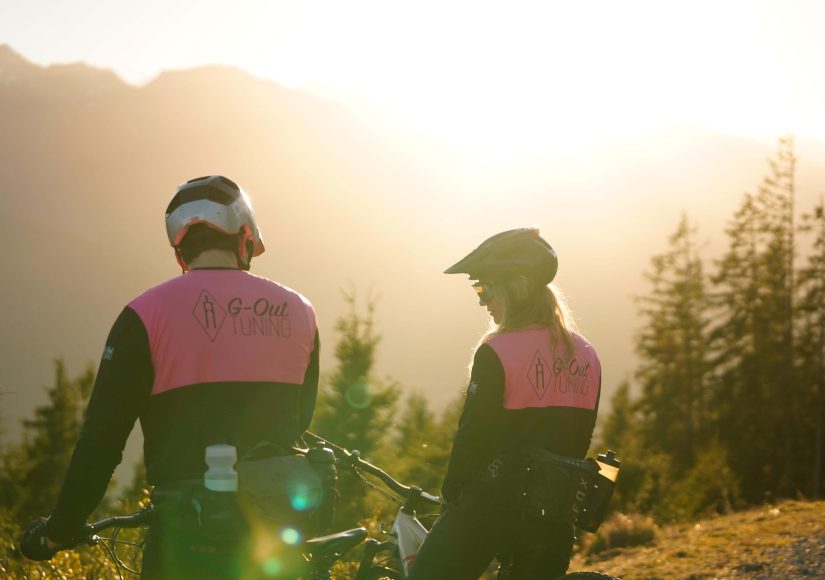 Mountainbiker im G-Out Tuning Outfit vor einer malerischen Berglandschaft bei Sonnenuntergang.