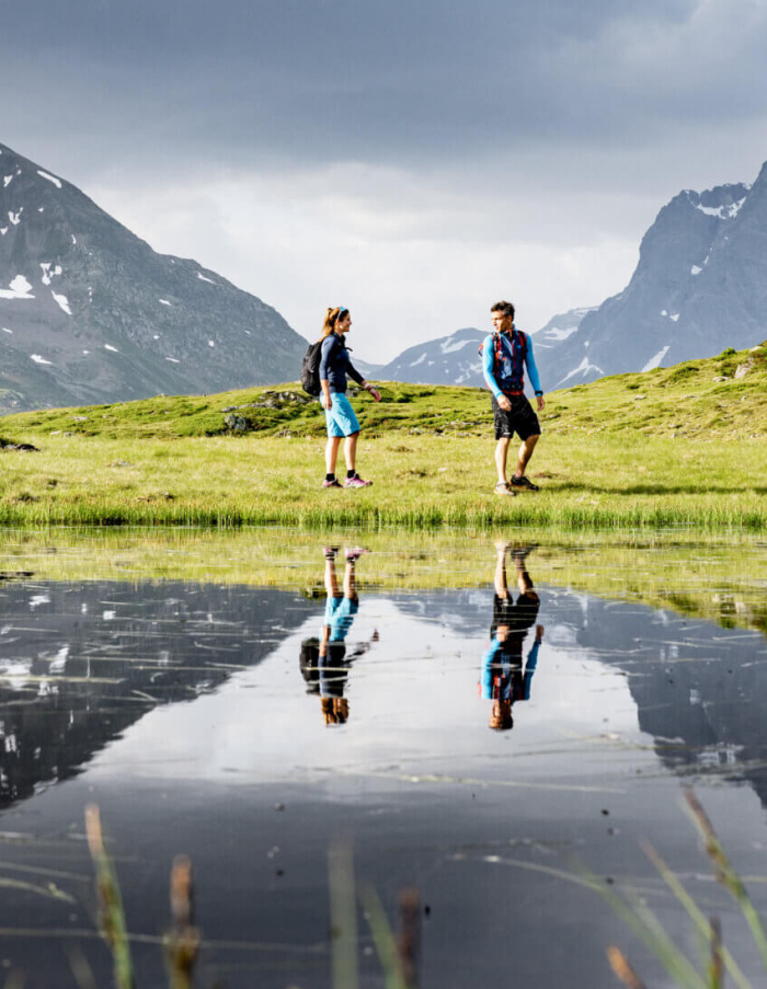 Wanderer erkunden eine alpine Landschaft mit spiegelndem Wasser und Bergen im Hintergrund.