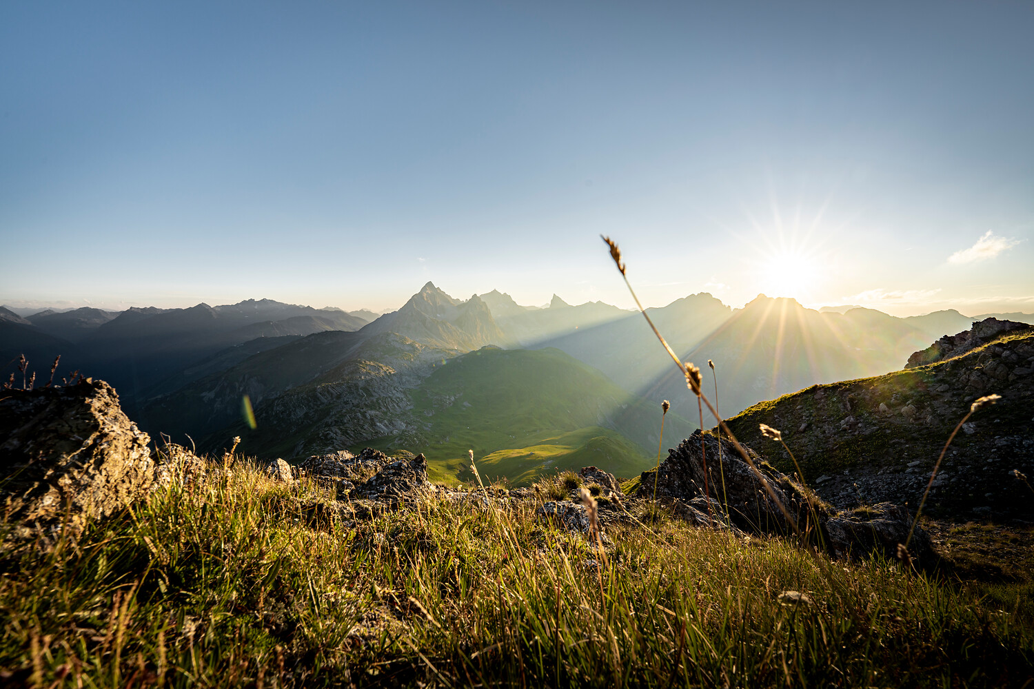 Sonnenlicht über alpinem Bergpanorama mit Felsen, Gräsern und grünen Tälern