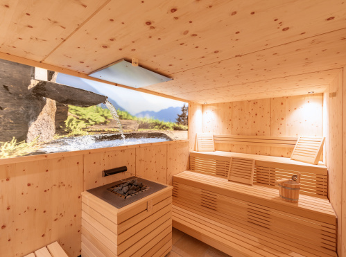 Helle Holzsauna mit Bänken, Saunaofen, Aufgusseimer und großem Bergmotiv mit Wasserfall