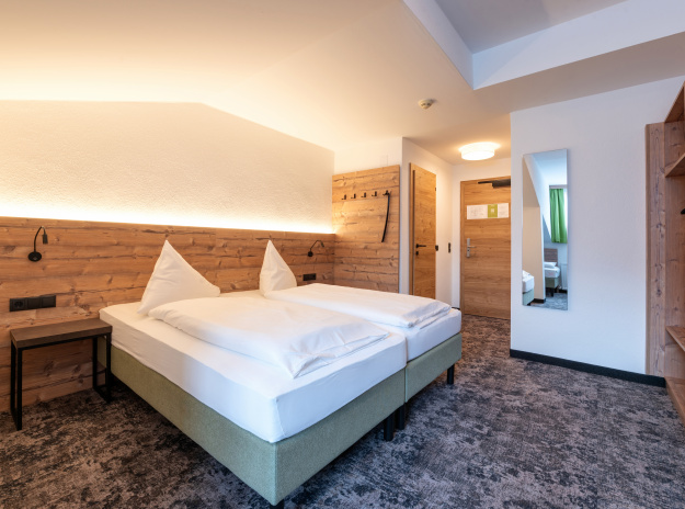 Hotelzimmer mit Doppelbett, Holzvertäfelung, warmem Licht und grauem Teppich