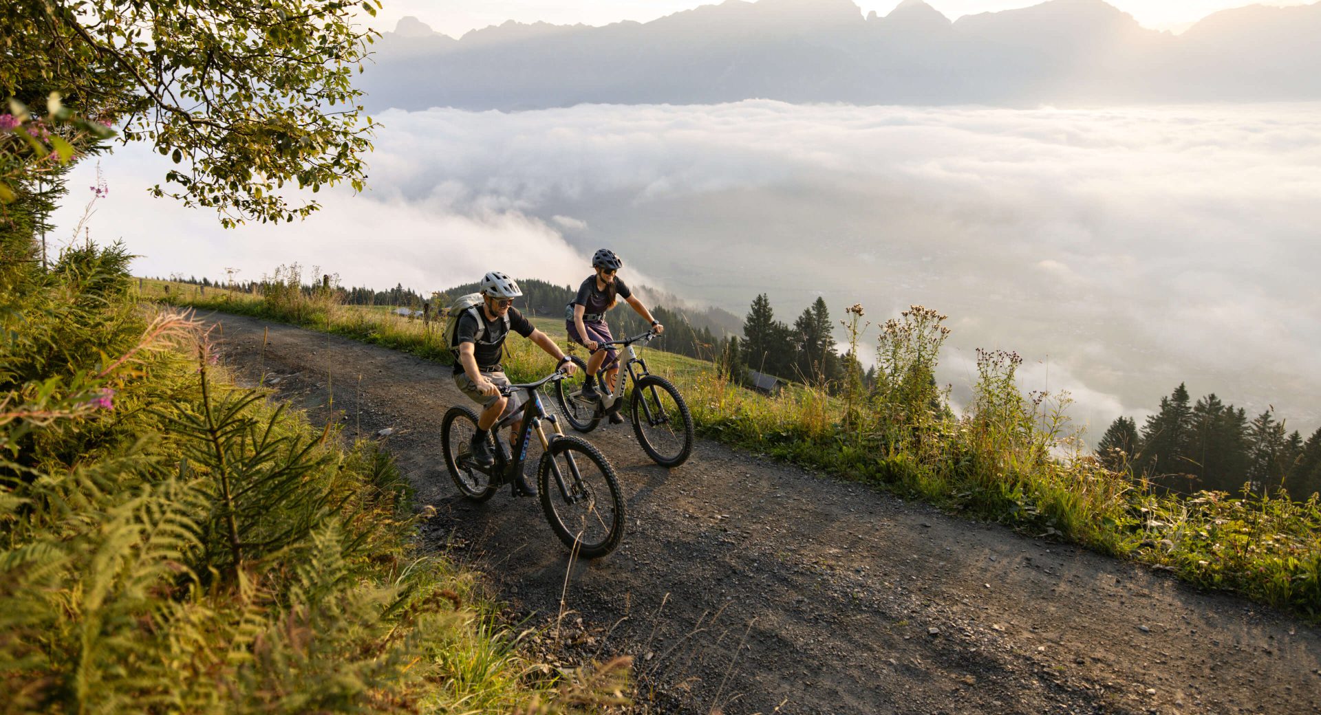 Zwei Mountainbiker fahren auf einem Waldweg mit Blick auf Nebel und Berge in Saalfelden.
