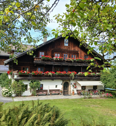 Hinterburghof mit Holzfassade, blumengeschmückten Balkonen, Sitzplatz und Wiese unter alten Bäumen