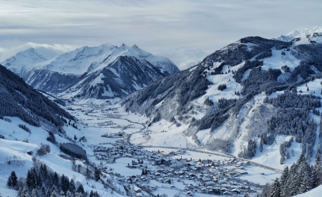 Verschneites Bergtal mit Dorf, bewaldeten Hängen und schneebedeckten Gipfeln
