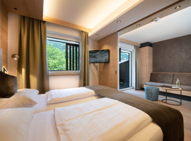 Modernes Hotelzimmer mit Doppelbett, Sitzecke, TV und Fenstern mit Blick ins Grüne