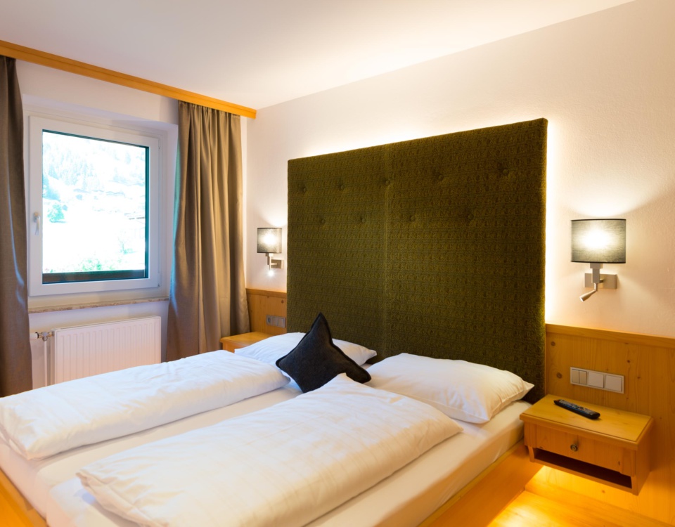 Doppelbett mit hohem dunkelgrünem Kopfteil in einem hellen Hotelzimmer mit Holzverkleidung