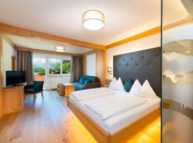 Helles Hotelzimmer mit Doppelbett, Sitzbereich, Fernseher und Balkon mit Bergblick