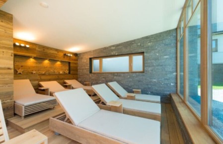 Heller Ruheraum mit Holzliegen, Steinwand und großen Fenstern