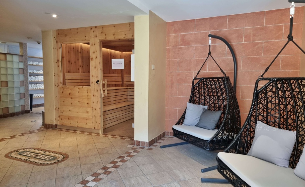 Wellnessbereich mit zwei Hängesesseln und geöffneter Holzsauna