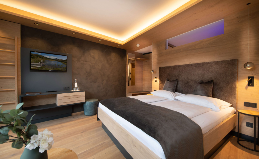 Modernes Hotelzimmer mit Doppelbett, Holzvertäfelung, Fernseher und warm indirekter Beleuchtung