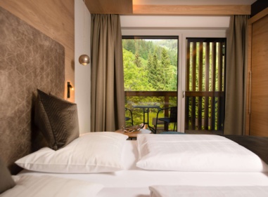 Modernes Hotelzimmer mit Doppelbett, Holzmöbeln und Balkon mit Blick ins Grüne