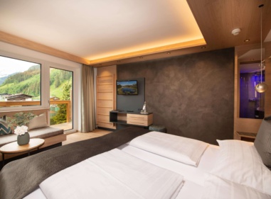 Modernes Hotelzimmer mit Doppelbett, Balkonblick auf grüne Berge und blau beleuchtetem Bad
