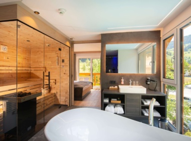 Freistehende Badewanne neben Sauna und großem Fenster mit Blick ins Grüne
