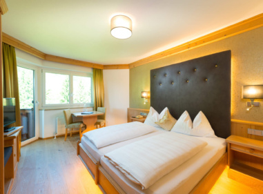 Helles Hotelzimmer mit Doppelbett, gepolstertem Kopfteil, Sitzecke und Balkonzugang